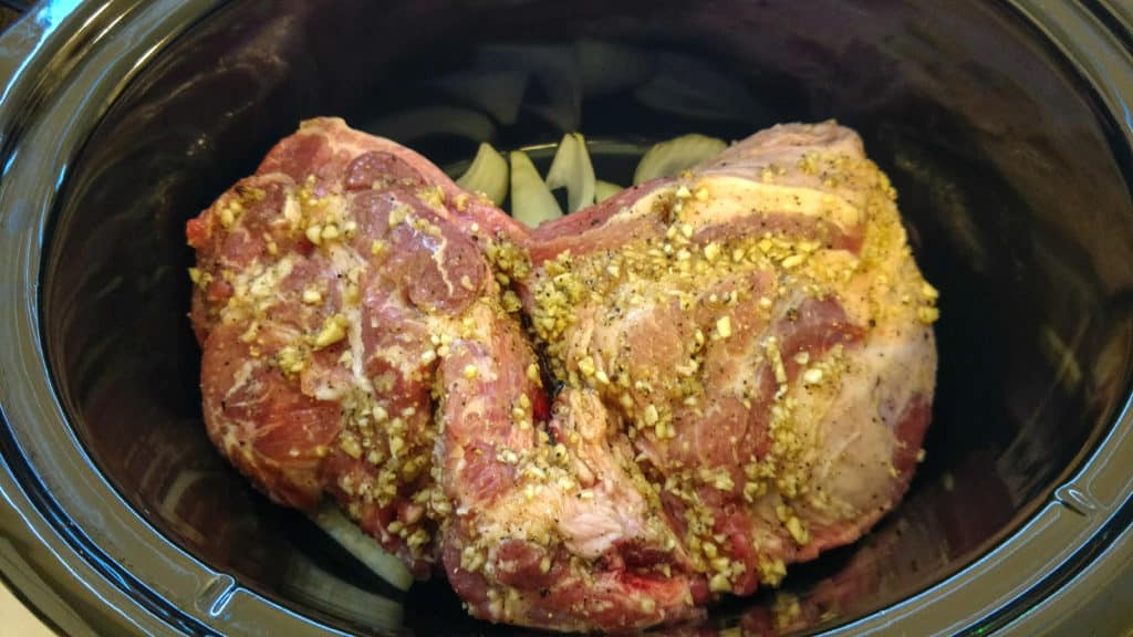 pork in a crockpot placed on sliced onions