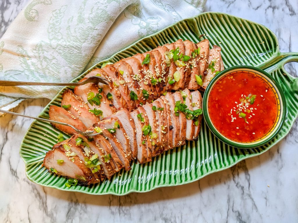 Chinese BBQ Pork (Char Sui) on a green leaf platter with sweet dipping sauce