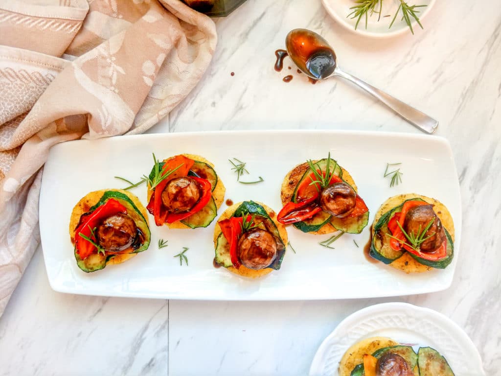 Grilled polenta and vegetable stacks on a white platter with balsamic drizzle