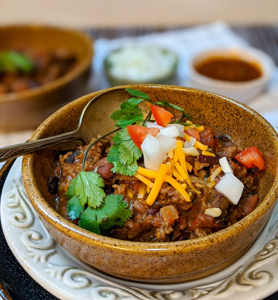 Beef chili in a bowl with cheese, onions and tomatoes