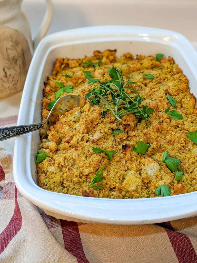 Southern cornbread dressing in a white baking dish, garnished with fresh herbs