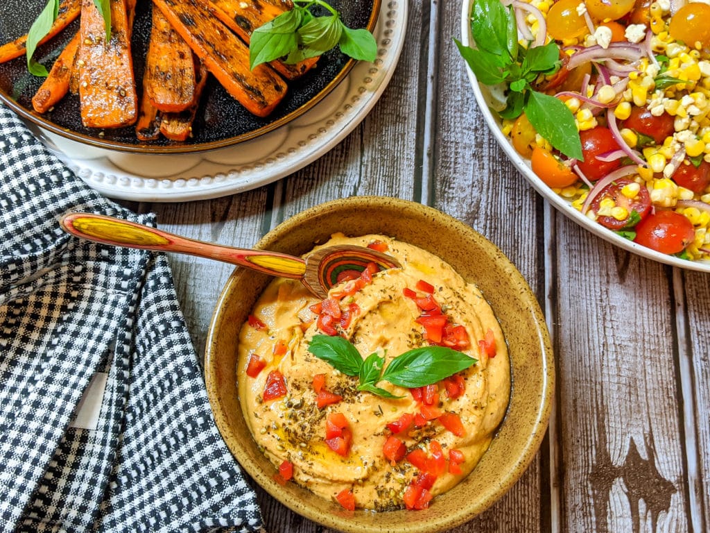 Bowl of hummus with grilled carrots and corn salad