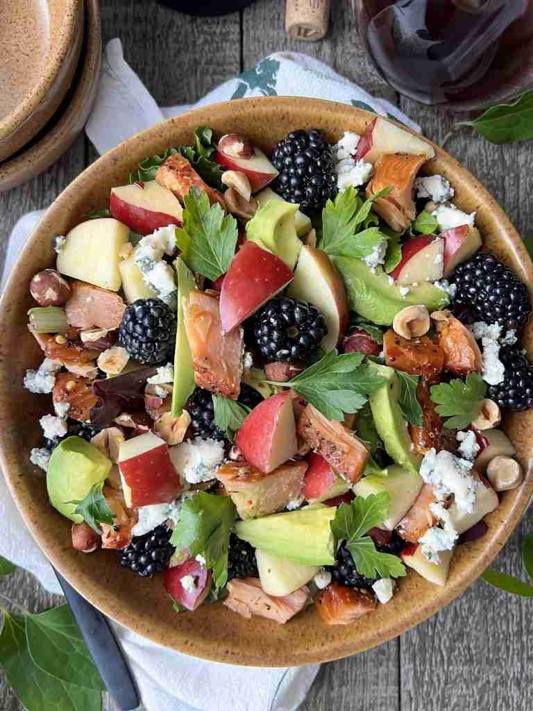 Salmon salad in a bowl with blackberries, apples, avocado, hazelnuts and blue cheese crumbles